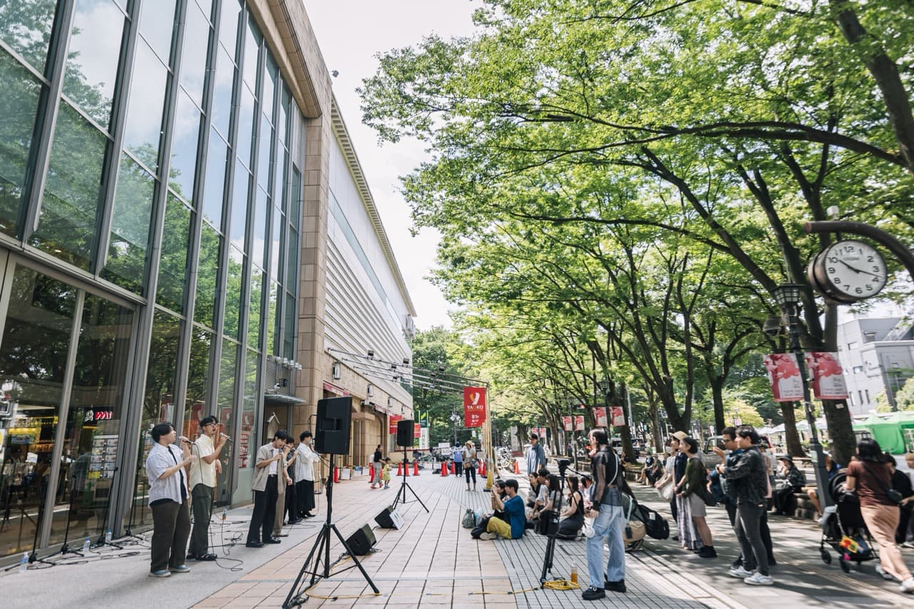 けやき並木の街路で歌うグループと、座って聴き入る観客